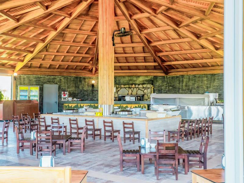 Área de comedor abierta con muchas mesas y sillas de madera bajo un techo alto de madera en la playa del hotel