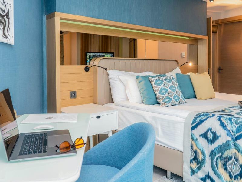 Habitación de hotel acogedora con tema azul, cama doble y área de trabajo con portátil.