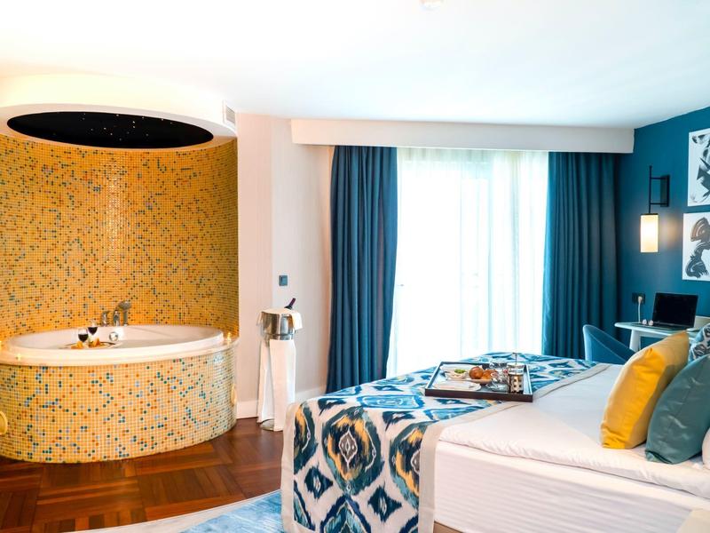 Habitación de hotel moderna con jacuzzi redondo, cortinas azules y cama doble acogedora.