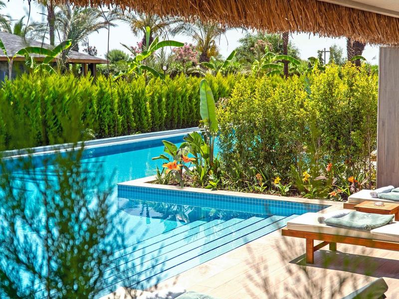 Piscina con estanque integrado y jardín tropical bajo techo de paja.