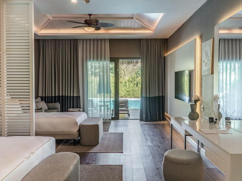 Habitación de hotel moderna con dos camas, área de descanso y ventana grande con cortinas.