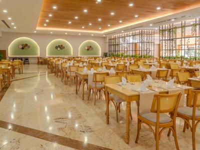 Spacious dining hall with wooden furniture, marble floor, and indirect ceiling lighting.