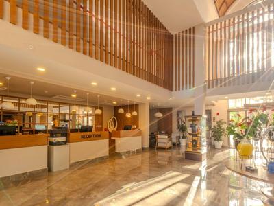 Spacious hotel lobby with reception and seating area, abundant natural light, and modern decor.