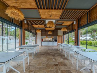 Bright open dining area with white tables and wooden ceiling lights in hotel.