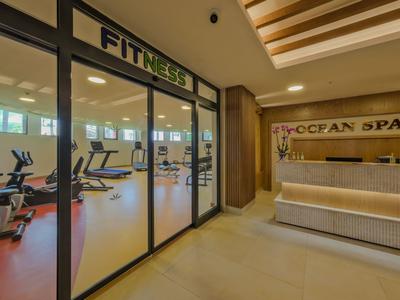 Sala fitness moderna dietro porte in vetro accanto a una reception spa con luce calda.