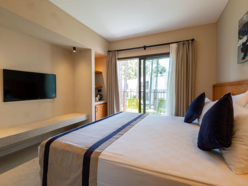 Bright hotel room with double bed, wall-mounted TV, and balcony access.