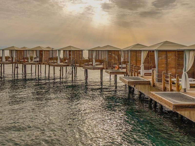 Overwater bungalows with wooden walkways over calm water at sunset.