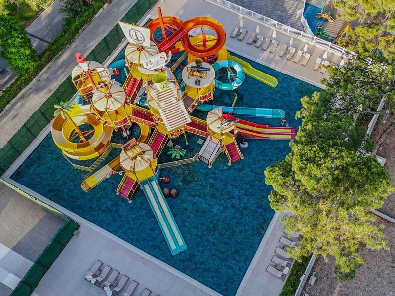 Colorful water playground in a pool surrounded by trees and lounge chairs