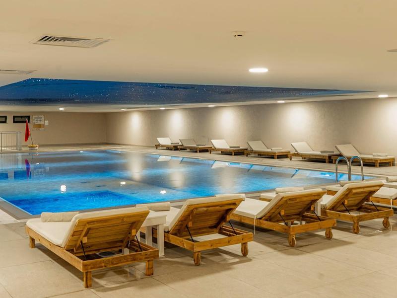 Indoor heated swimming pool with lounge chairs and soft lighting in a hotel.