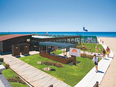 Ristorante sulla spiaggia con passerelle in legno, prati e vista sulla spiaggia sabbiosa e il mare.