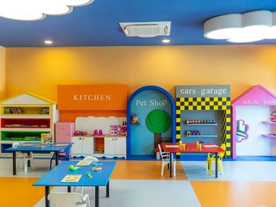 Angolo bambini colorato con cucina giocattolo, garage e tavoli per attività in una stanza luminosa.