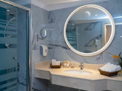 Bagno moderno con specchio rotondo illuminato, lavabo e cabina doccia.