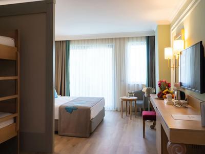 Camera d'hotel luminosa con letto matrimoniale, letti a castello, scrivania e TV a parete.