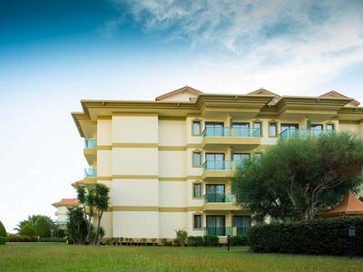 Edificio dell'hotel giallo con più piani e alberi in primo piano sotto un cielo soleggiato.