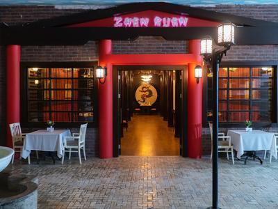 Ingresso di un ristorante asiatico con colonne rosse e tavoli apparecchiati a sinistra e a destra.