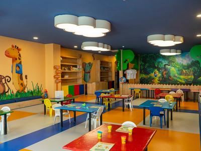 Kleurrijke speelkamer voor kinderen met dierenmuurschilderingen, tafels en kleine stoelen in een hotelomgeving.