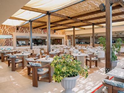 Licht, open restaurant met rijen tafels, houten meubels en planten.