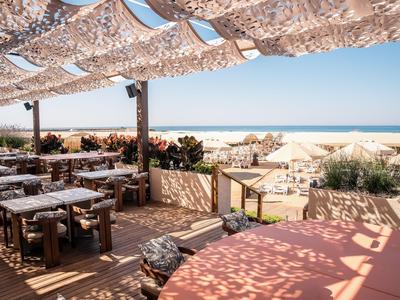 Open restaurant met houten meubels en zonnescherm bij het strand met zeezicht.