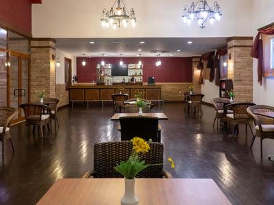 Licht hotelrestaurant met houten vloer, tafels, stoelen en een lange bar met warme verlichting.
