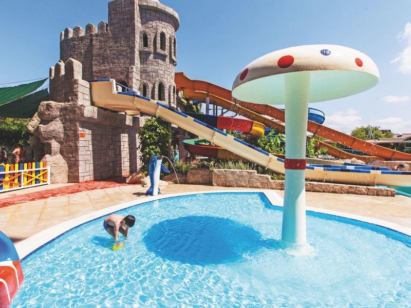 Bambini giocano in una piscina con scivoli e fungo d'acqua in un parco vacanze.