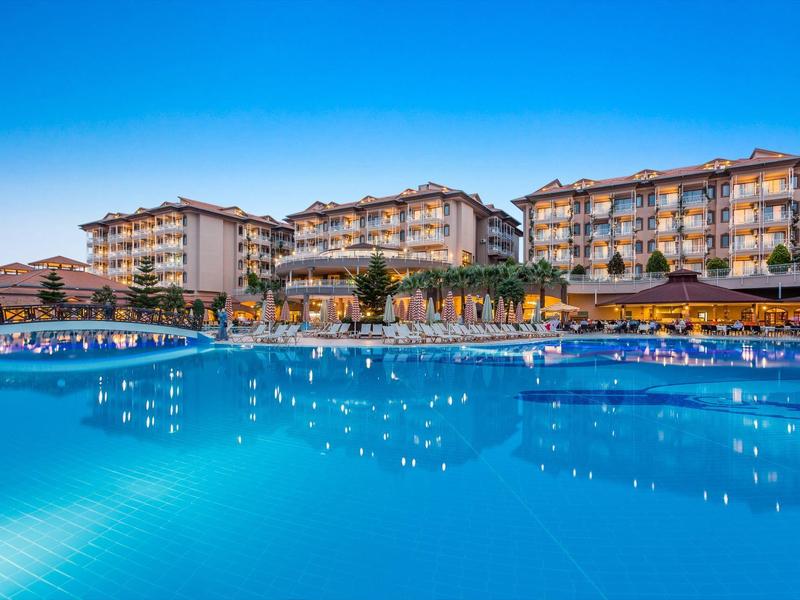 Hotel di lusso con grande piscina esterna sotto un cielo blu al crepuscolo.