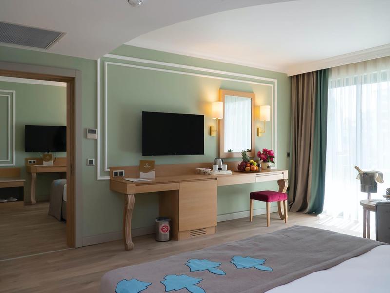 Camera d'hotel moderna con grande televisore, scrivania e finestra con vista esterna.