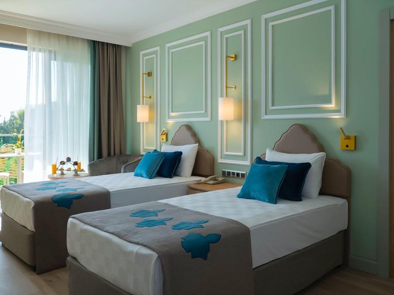 Camera d'hotel luminosa con due letti singoli, lampade da parete moderne e balcone con vista.