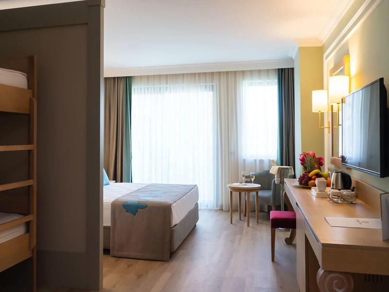 Camera d'hotel luminosa con letto matrimoniale, letti a castello, scrivania e TV a parete.