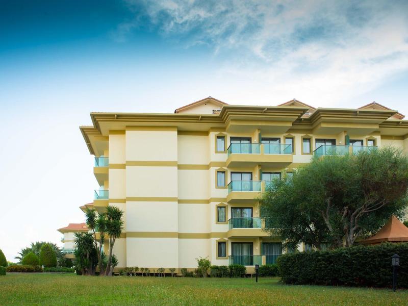 Edificio dell'hotel giallo con più piani e alberi in primo piano sotto un cielo soleggiato.