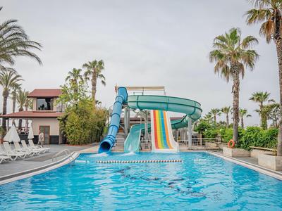 Piscine avec toboggans aquatiques et palmiers dans un hôtel sous un ciel nuageux