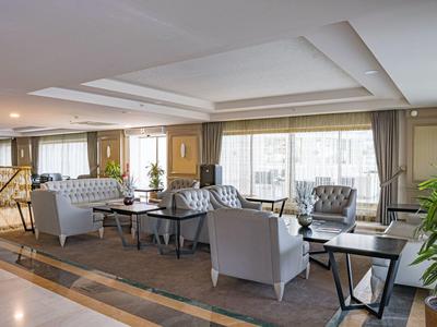 Sala de estar luminosa de hotel con sillones modernos, sofás y grandes ventanas con cortinas.