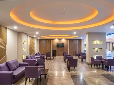 Vestíbulo de hotel moderno con sofás morados, sillas y luz cálida en el techo.