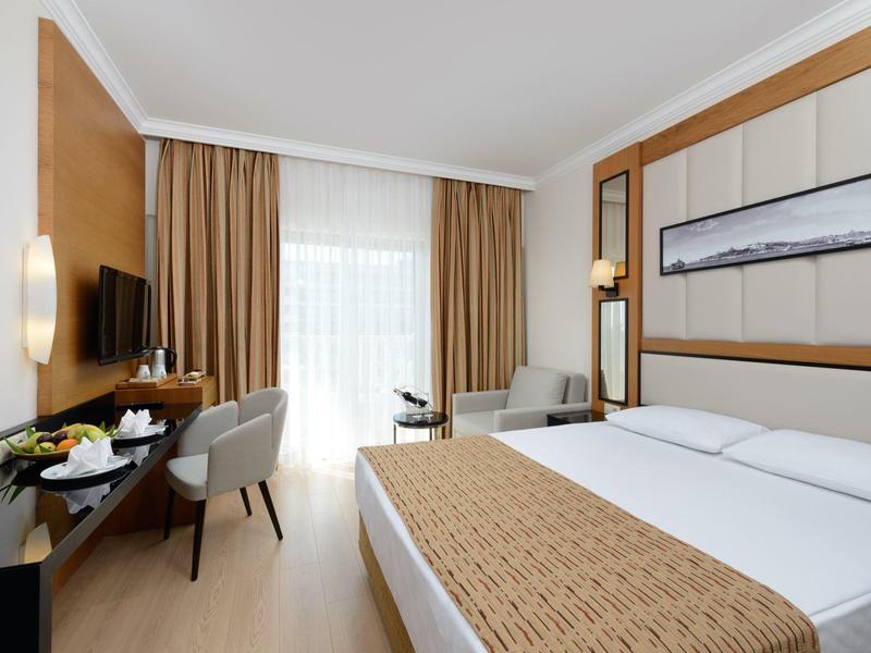 Habitación de hotel moderna con cama grande, escritorio, silla y balcón con luz natural.