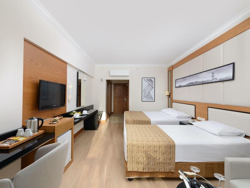 Habitación de hotel moderna con dos camas, televisor de pantalla plana y muebles de madera clara.