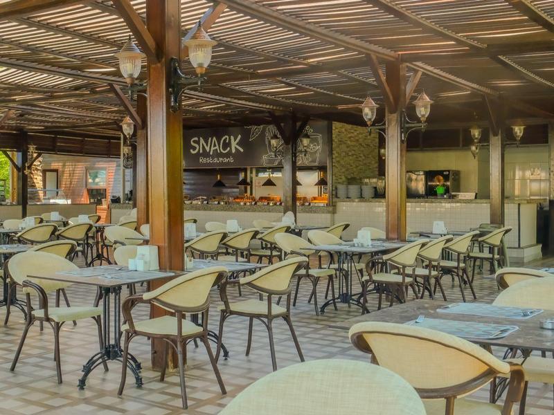 Área de restaurante al aire libre con mesas y sillas bajo un techo de madera en un hotel.