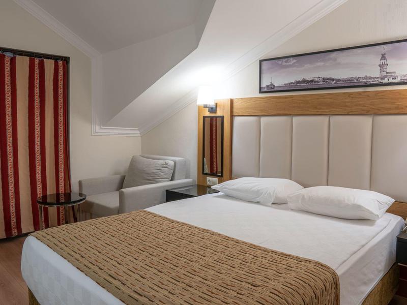 Habitat acogedor de hotel con cama grande, cabecera acolchada y un sillón bajo techo inclinado.