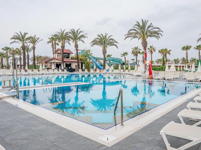 Una gran piscina con toboganes de agua, rodeada de palmeras y tumbonas en un día nublado.
