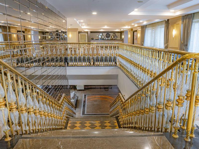 Escalera elegante de hotel con barandilla dorada y suelo de mármol en un interior luminoso.