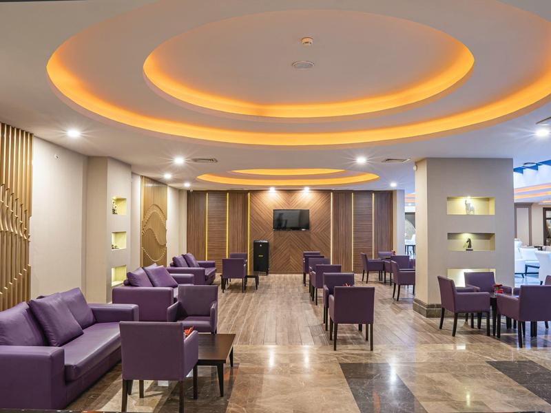 Vestíbulo de hotel moderno con sofás morados, sillas y luz cálida en el techo.