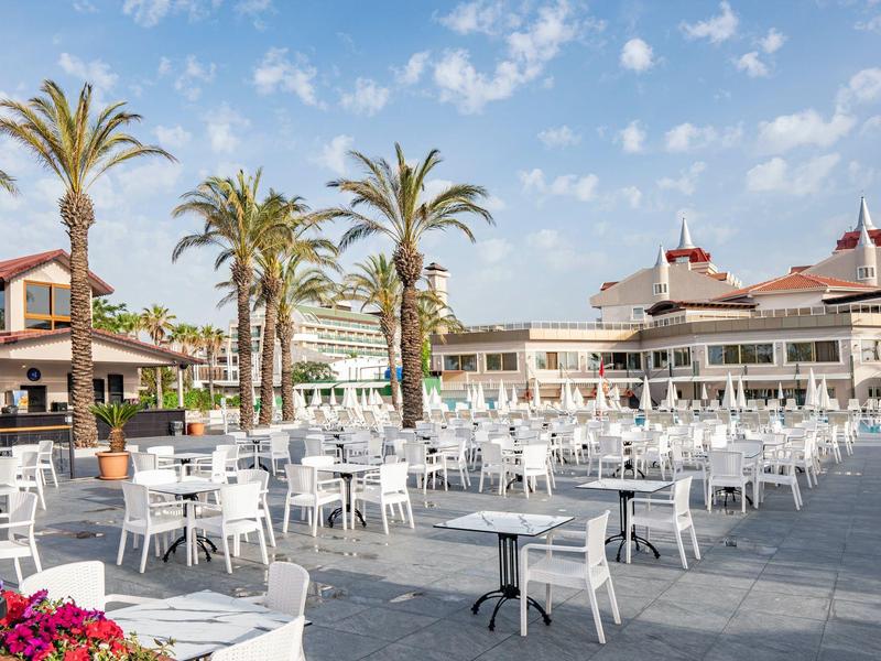 Amplia terraza de hotel con mesas y sillas blancas bajo cielo azul y palmeras.