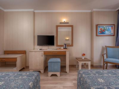 Habitación de hotel con dos camas, TV, taburete, espejo y silla en tonos cálidos.