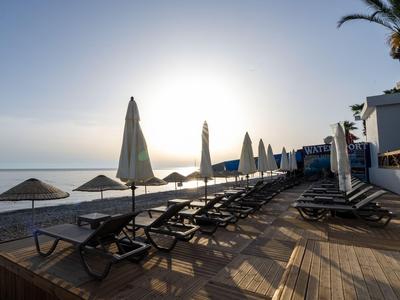 Rangée de chaises longues vides et parasols fermés sur une terrasse en bois à la plage au lever du soleil.