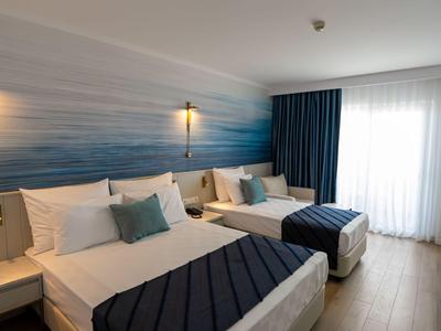 Chambre d'hôtel moderne avec deux lits doubles, accents bleus et grande fenêtre.