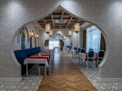 Une salle à manger d'hôtel élégante avec une arche orientale et des zones de sièges bleues et rouges.