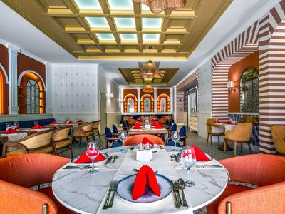 Nowoczesny bar hotelowy z jasnymi, kolorowymi krzesłami i ozdobnym oświetleniem sufitowym.