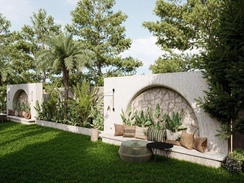 Jardín con césped verde, plantas mediterráneas y muros blancos con arcos bajo un cielo soleado.