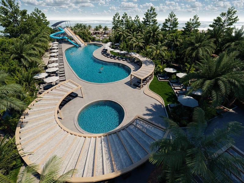 Piscina de hotel de lujo con forma orgánica, rodeada de palmeras y tumbonas bajo cielo nublado.