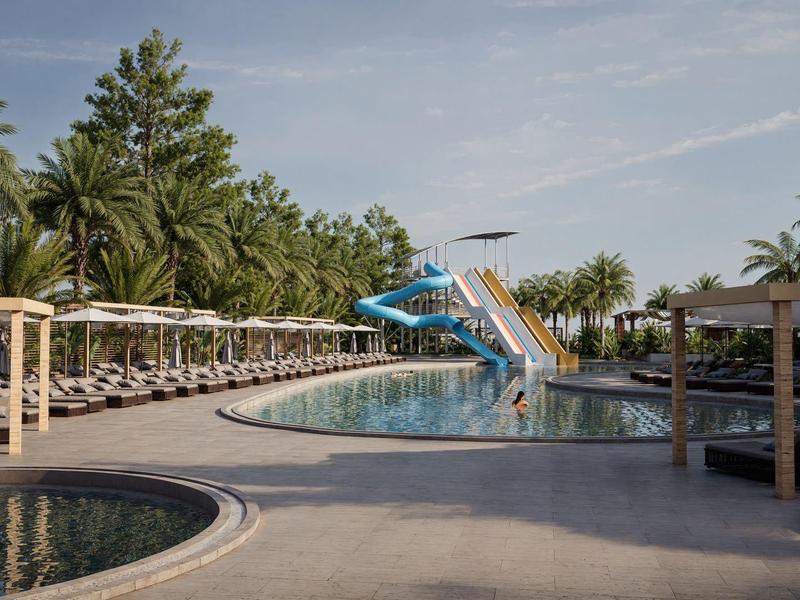 Gran área de piscina con toboganes de agua, tumbonas y palmeras en un resort.