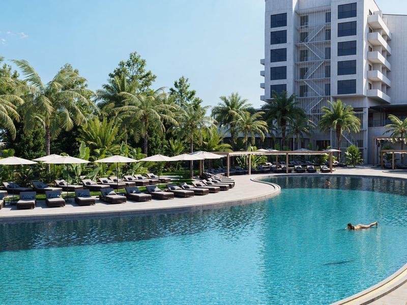 Gran piscina del hotel con tumbonas y palmeras, con un edificio de varios pisos al fondo.