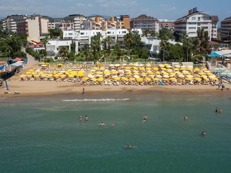 Pláž se žlutými slunečníky před hotelovou oblastí a lidmi ve vodě.